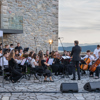 Mladi simfonijski orkestar nastupa na otvorenom ispred kamenog zida.